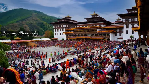 Wide view of the festival ground and dzong with spectators and dancers