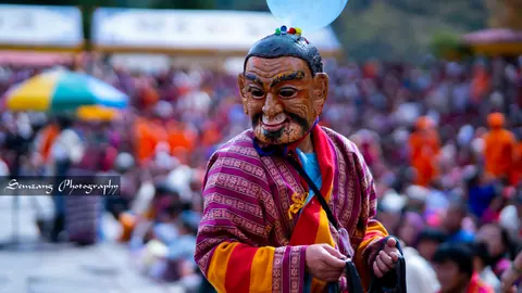 Smiling atsara in a mask and striped gho amid the festival crowd