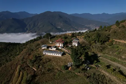 Aerial view of a temple on a forested ridge above misty valleys