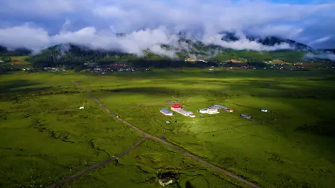 Aerial view of a green valley with low clouds and mountains