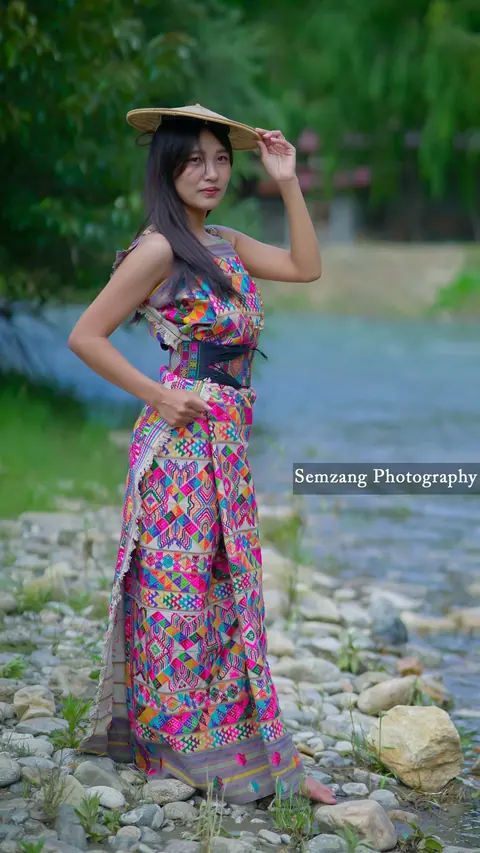 Woman in a traditional dress and bamboo hat standing by a rocky stream