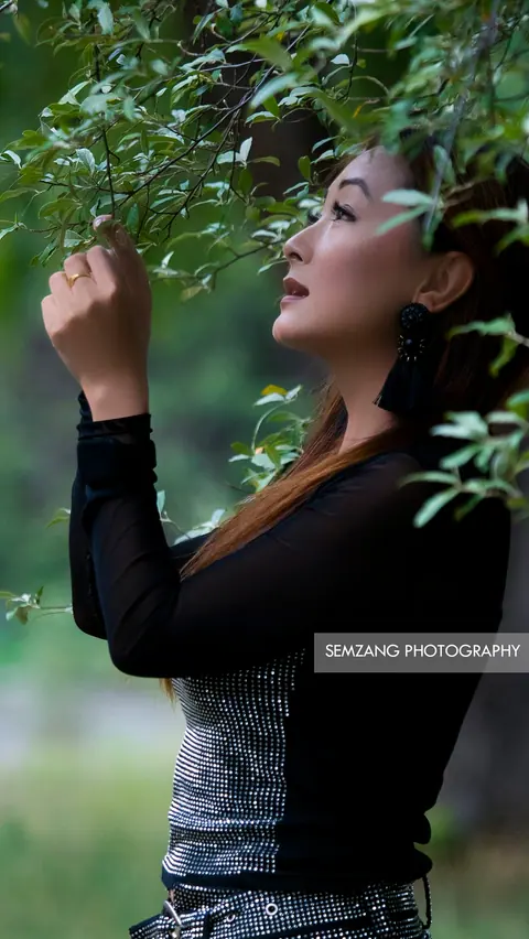Woman in a black top reaching toward leafy branches