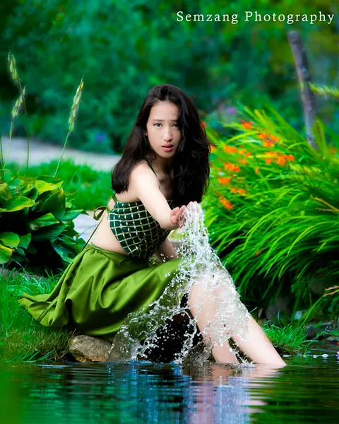 Woman in a green dress sitting by a stream with splashing water