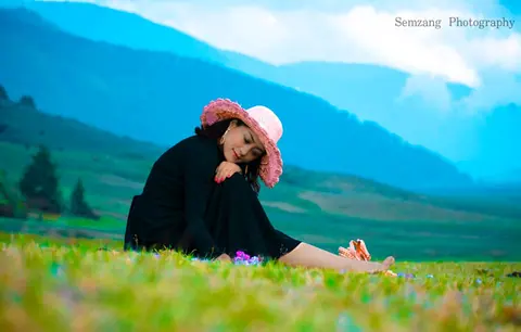 Woman in a pink hat sitting in a green valley meadow