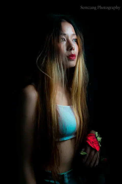 Portrait of a woman with long hair and a turquoise top holding a red flower