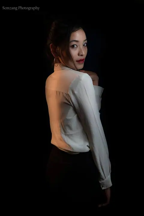 Low-key portrait of a woman looking over her shoulder in a white top