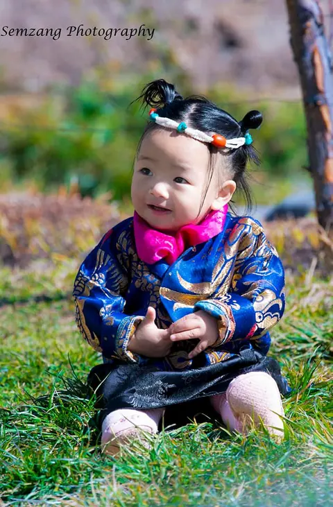 Smiling toddler in traditional clothing and hair ornaments sitting on grass