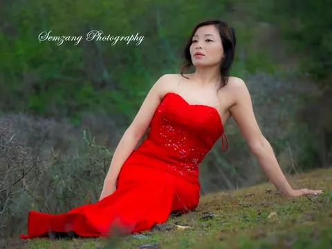 Woman in a red dress seated on a grassy hillside