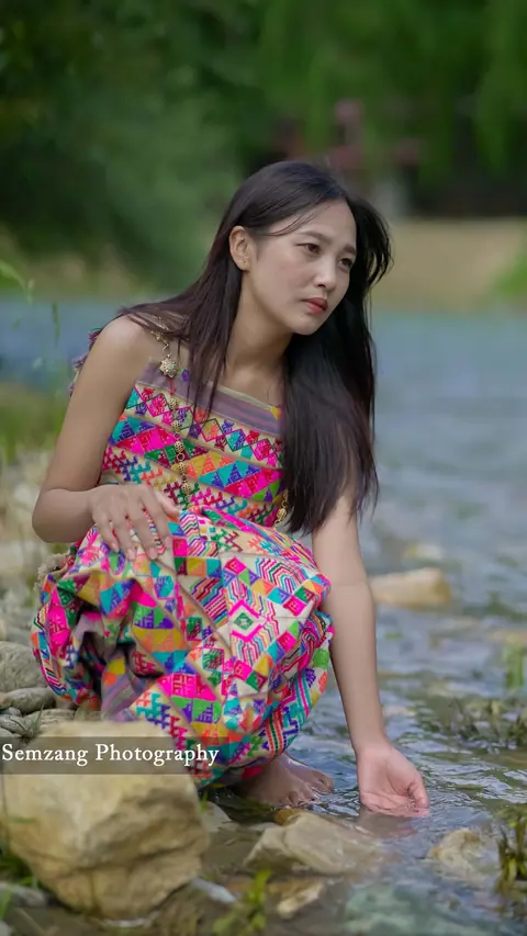 Woman in a colourful dress crouching by a river