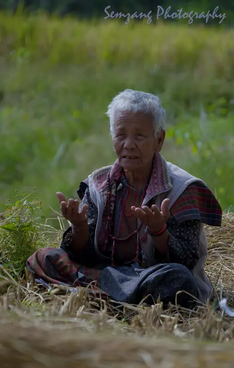 Elderly woman with hands raised sitting on straw