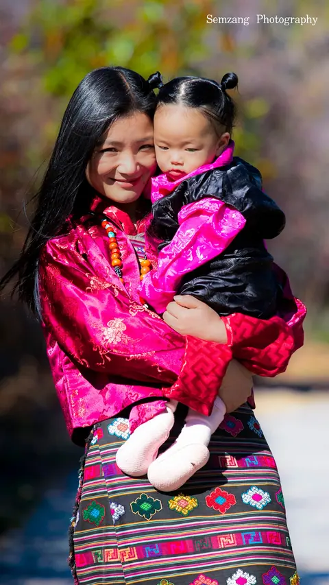 Woman in a pink jacket carrying a toddler by a stream
