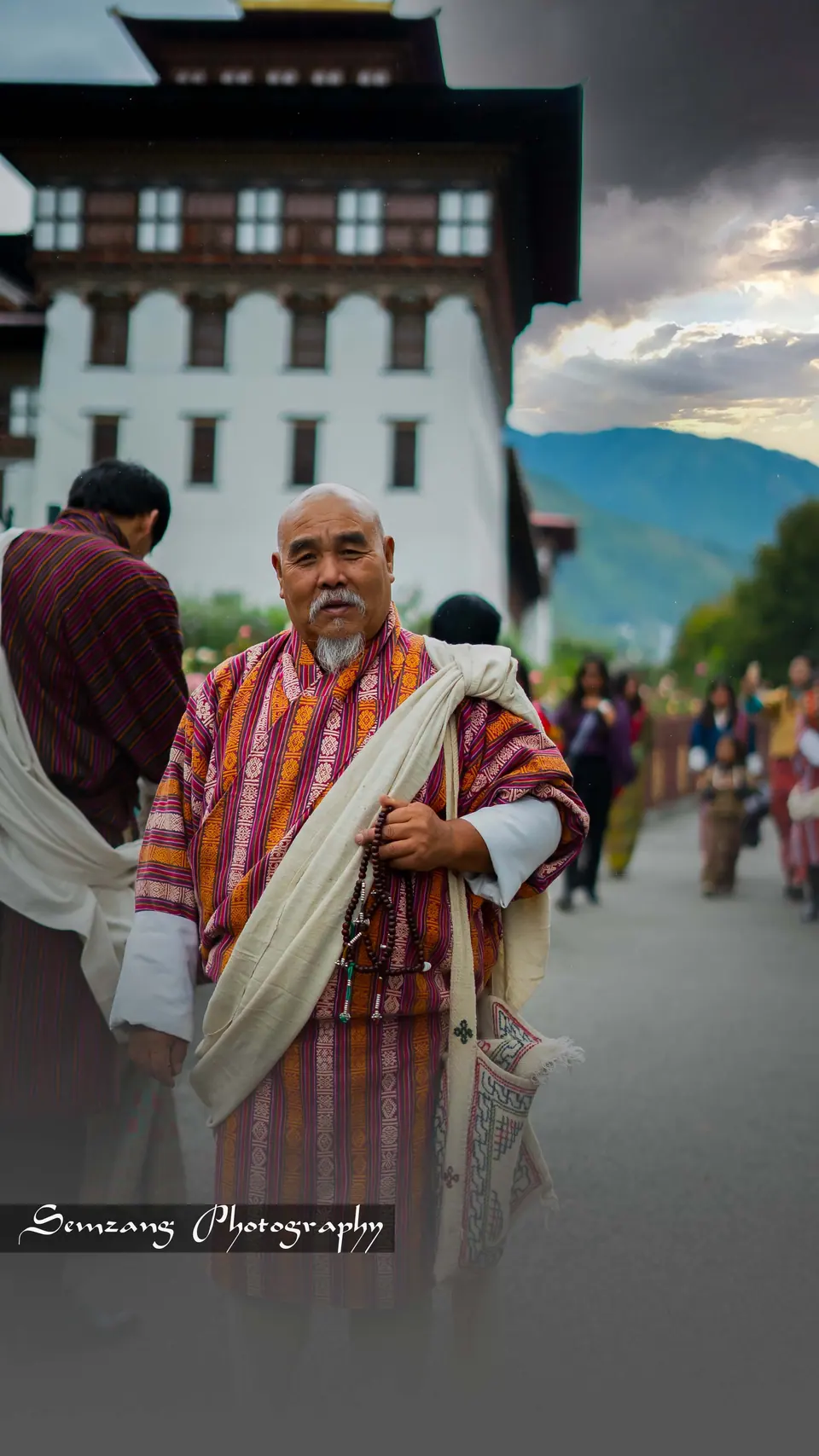 Man in a traditional gho and scarf on a street in front of a dzong